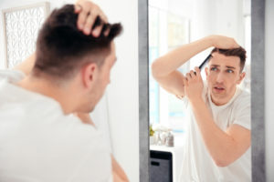薄毛を気にしながら鏡を見てヘアスタイルを整える男性